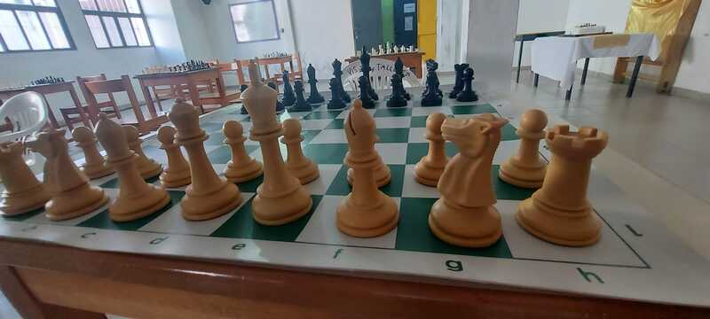 Tablero de ajedrez armado en una mesa, fichas de color crema y negras 